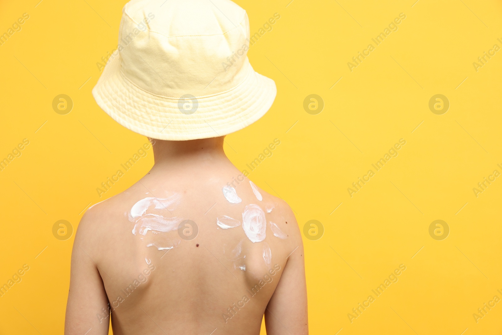 Little boy with sun protection cream on his skin against yellow background, back view. Space for text Photo of Little boy with sun protection cream on his skin against yellow background, back view. Space for text