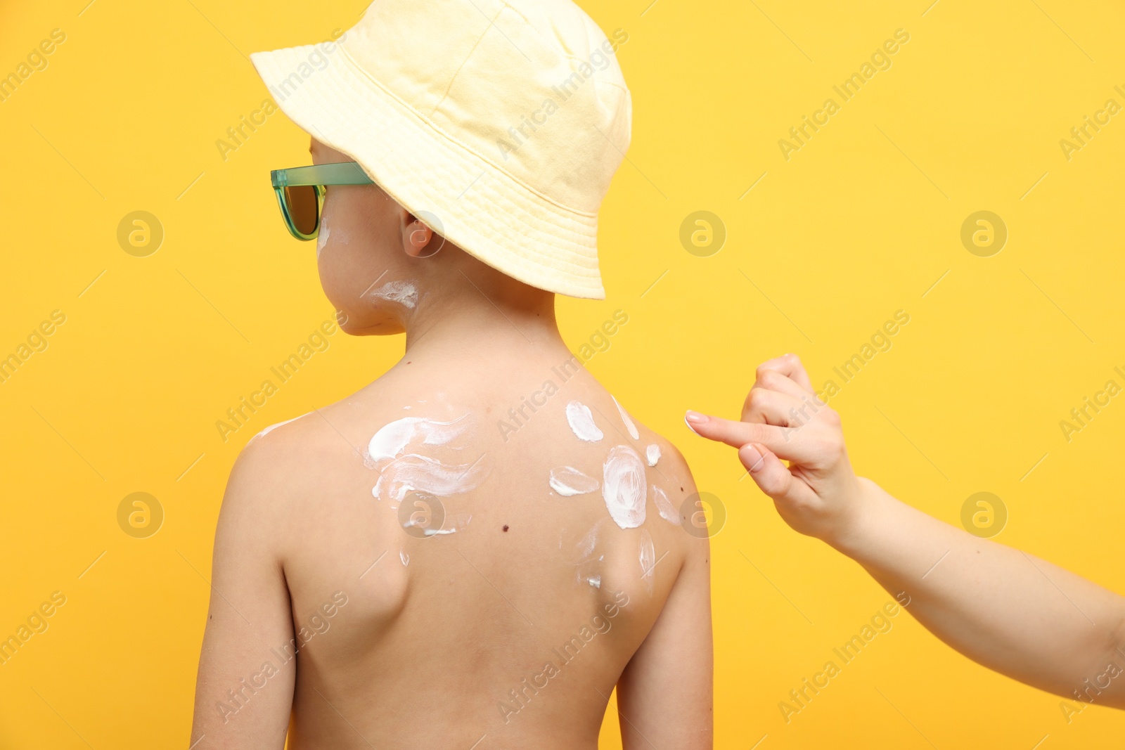 Mother applying sun protection cream onto her son's skin on yellow background, closeup Photo of Mother applying sun protection cream onto her son's skin on yellow background, closeup