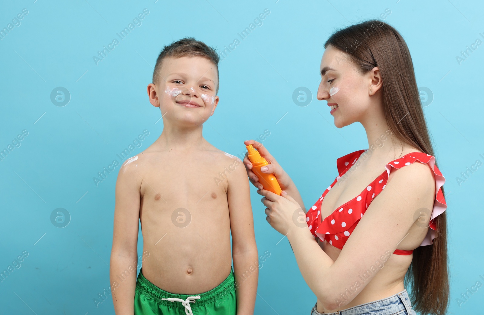 Mother applying sun protection cream onto her son's skin on light blue background Photo of Mother applying sun protection cream onto her son's skin on light blue background