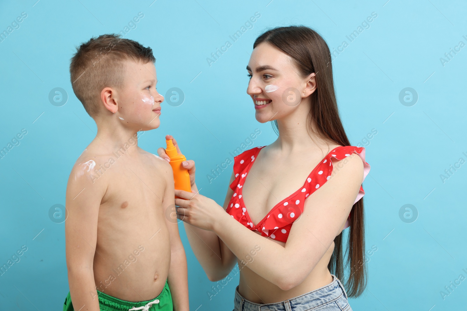 Mother applying sun protection cream onto her son's skin on light blue background Photo of Mother applying sun protection cream onto her son's skin on light blue background