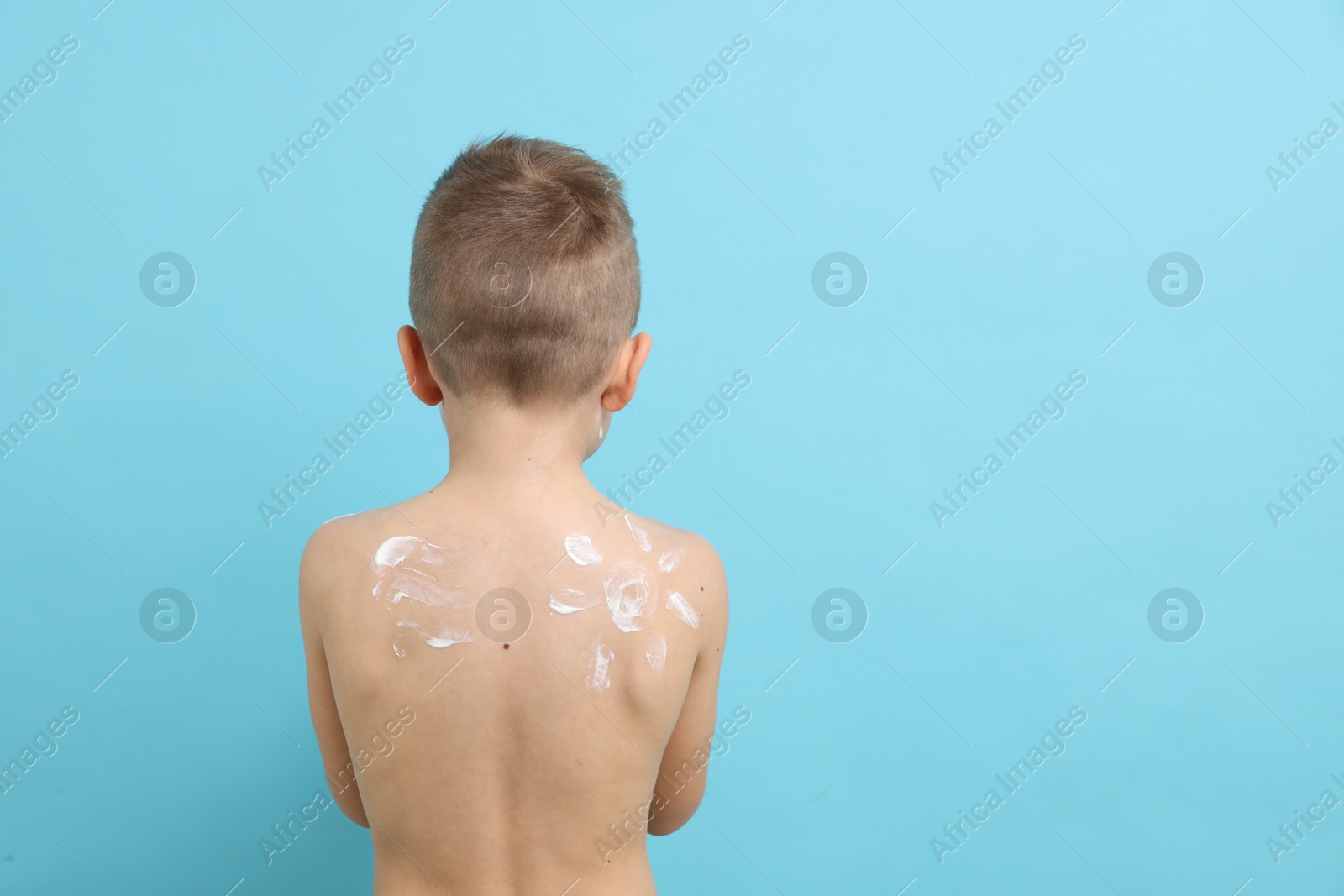 Little boy with sun protection cream on his skin against light blue background, back view. Space for text Photo of Little boy with sun protection cream on his skin against light blue background, back view. Space for text