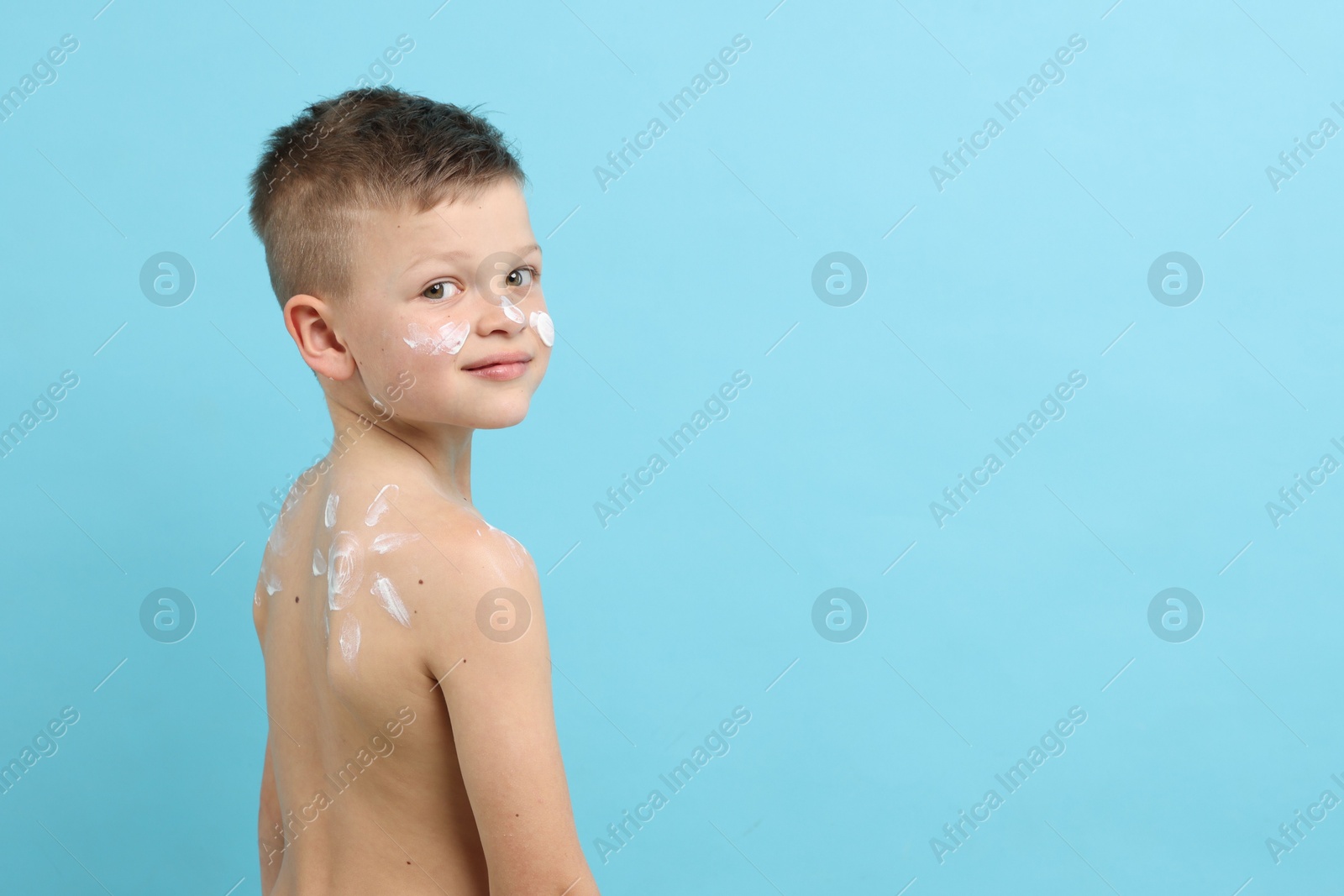 Little boy with sun protection cream on his skin against light blue background, space for text Photo of Little boy with sun protection cream on his skin against light blue background, space for text