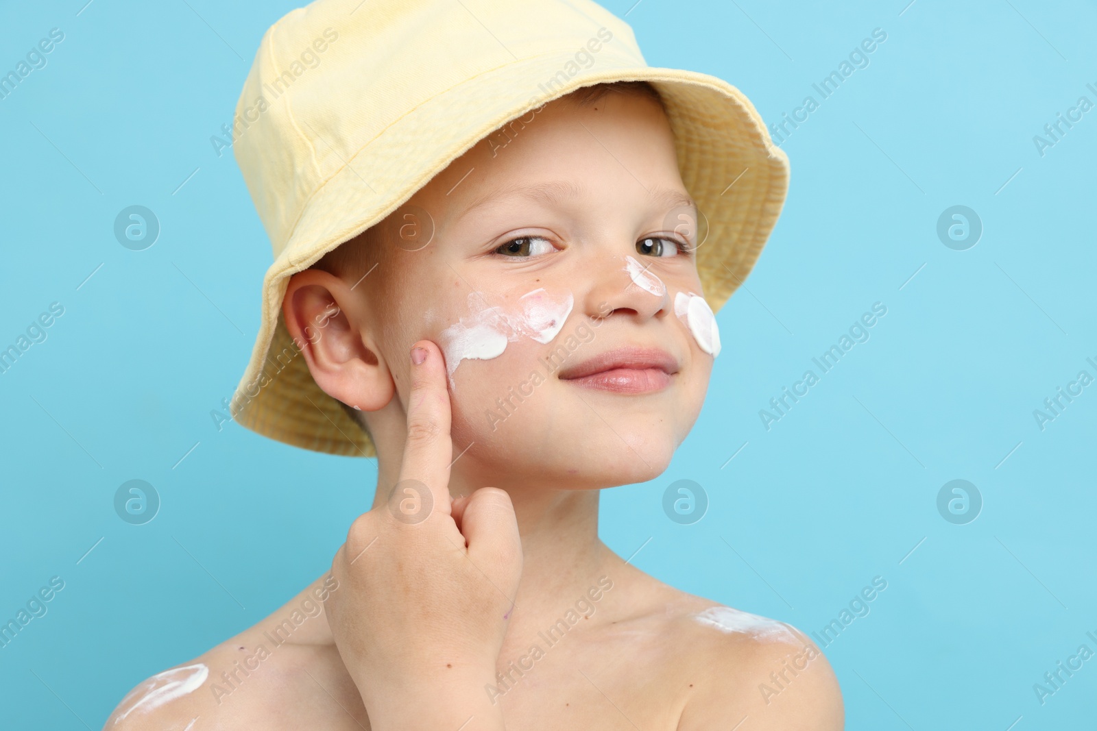 Little boy applying sun protection cream onto his skin on light blue background Photo of Little boy applying sun protection cream onto his skin on light blue background