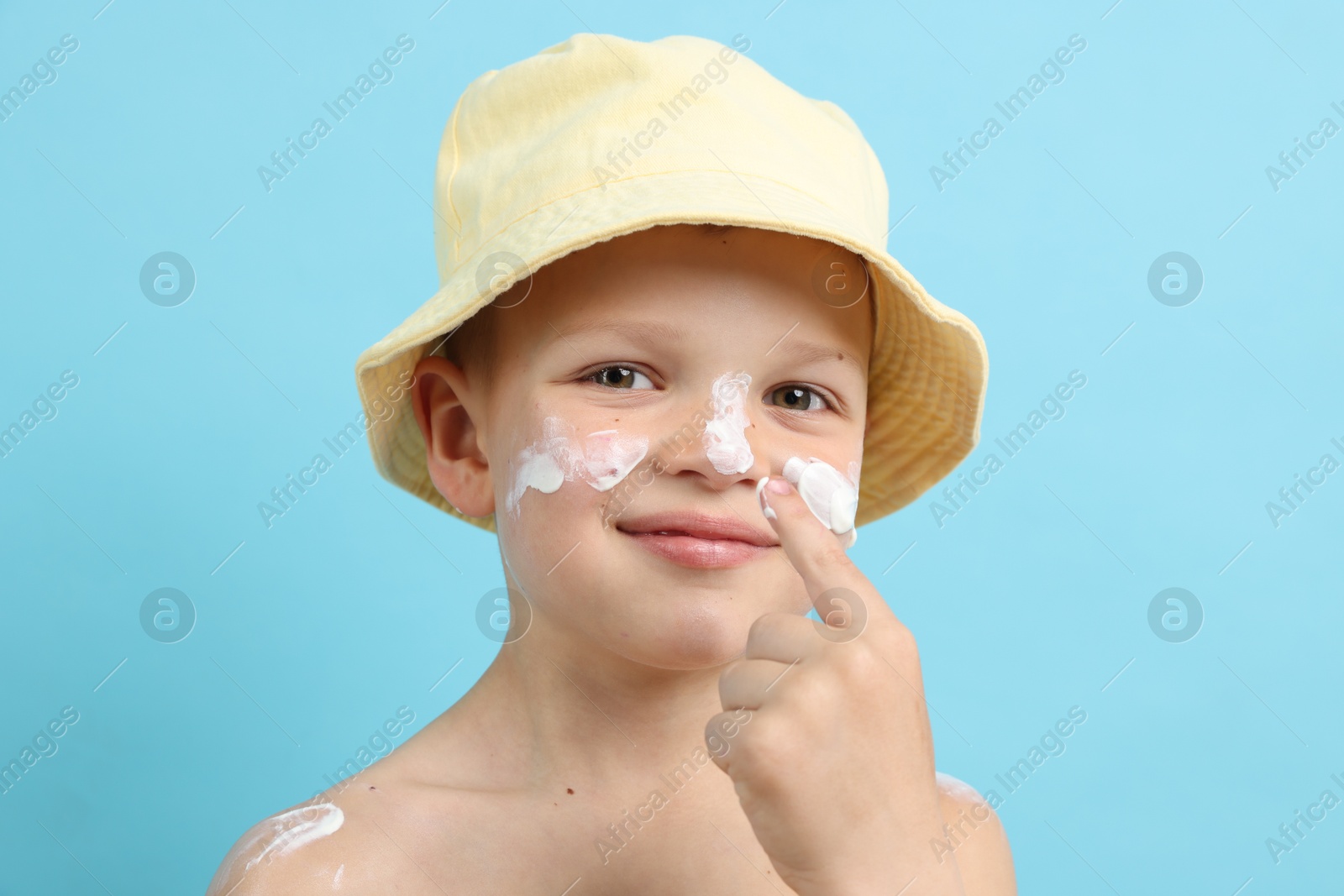 Little boy applying sun protection cream onto his skin on light blue background Photo of Little boy applying sun protection cream onto his skin on light blue background