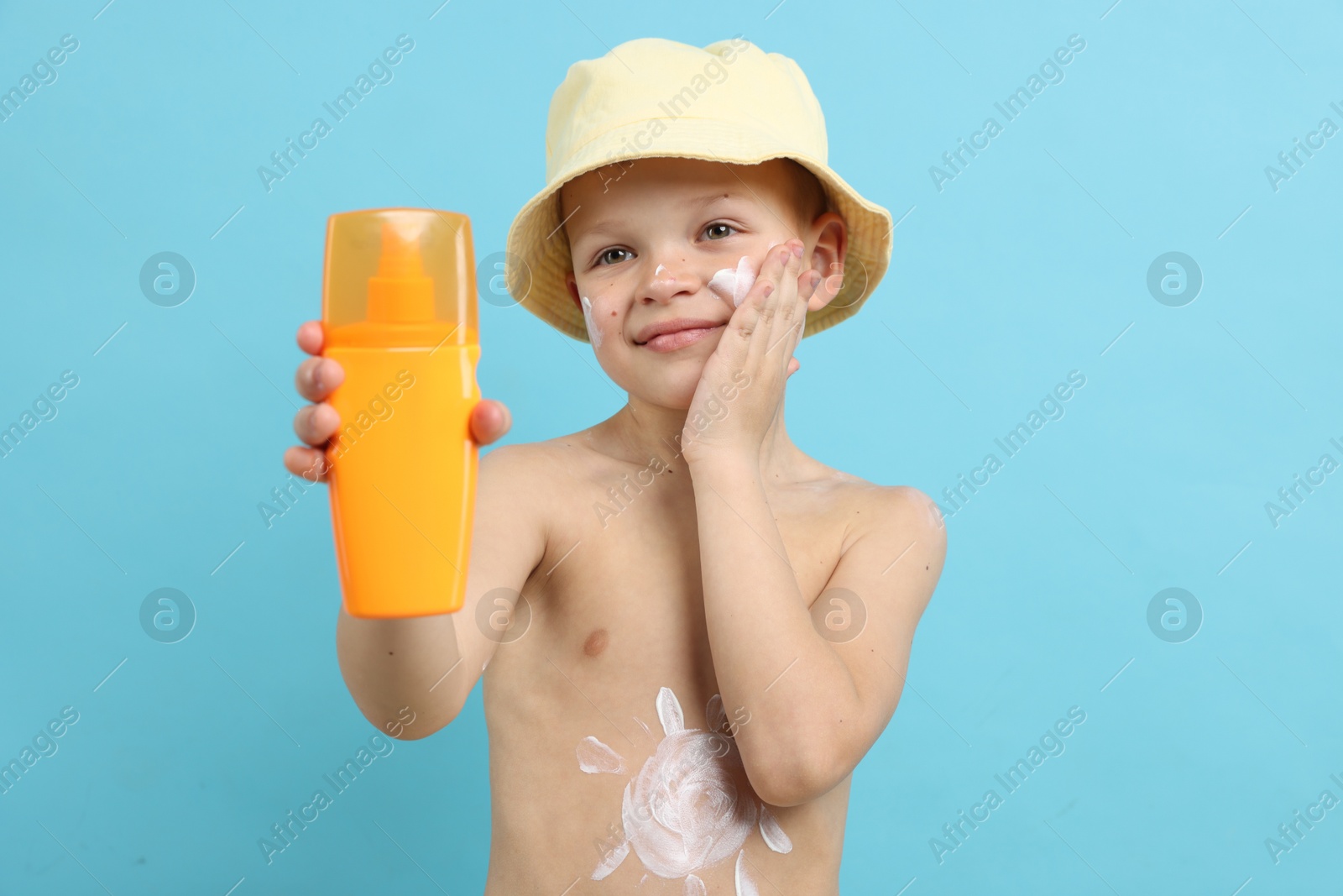 Little boy with tube applying sun protection cream onto his skin on light blue background Photo of Little boy with tube applying sun protection cream onto his skin on light blue background