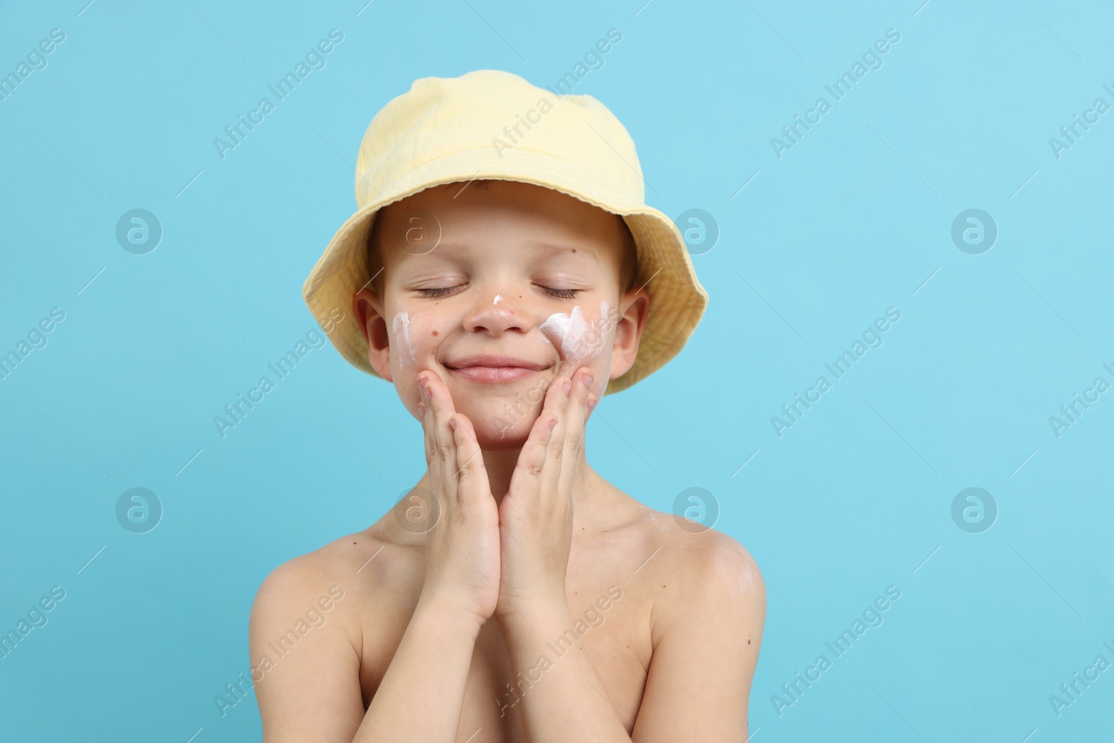 Little boy applying sun protection cream onto his skin on light blue background Photo of Little boy applying sun protection cream onto his skin on light blue background