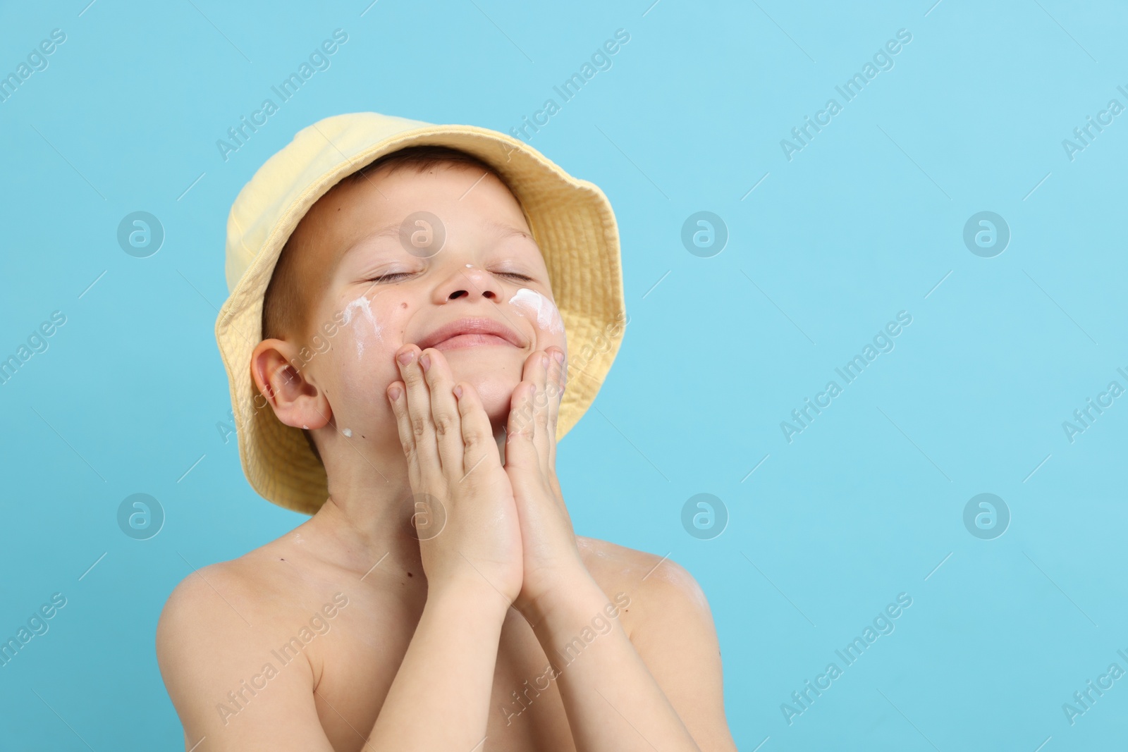 Little boy applying sun protection cream onto his skin on light blue background, space for text Photo of Little boy applying sun protection cream onto his skin on light blue background, space for text