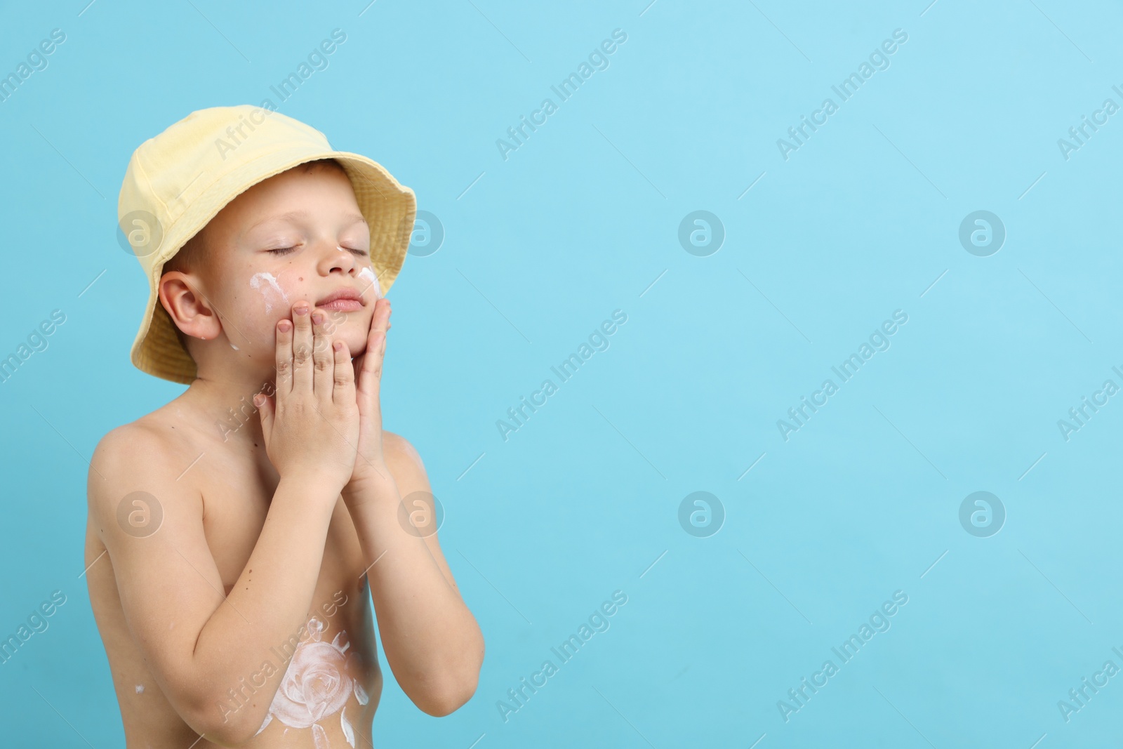 Little boy applying sun protection cream onto his skin on light blue background, space for text Photo of Little boy applying sun protection cream onto his skin on light blue background, space for text