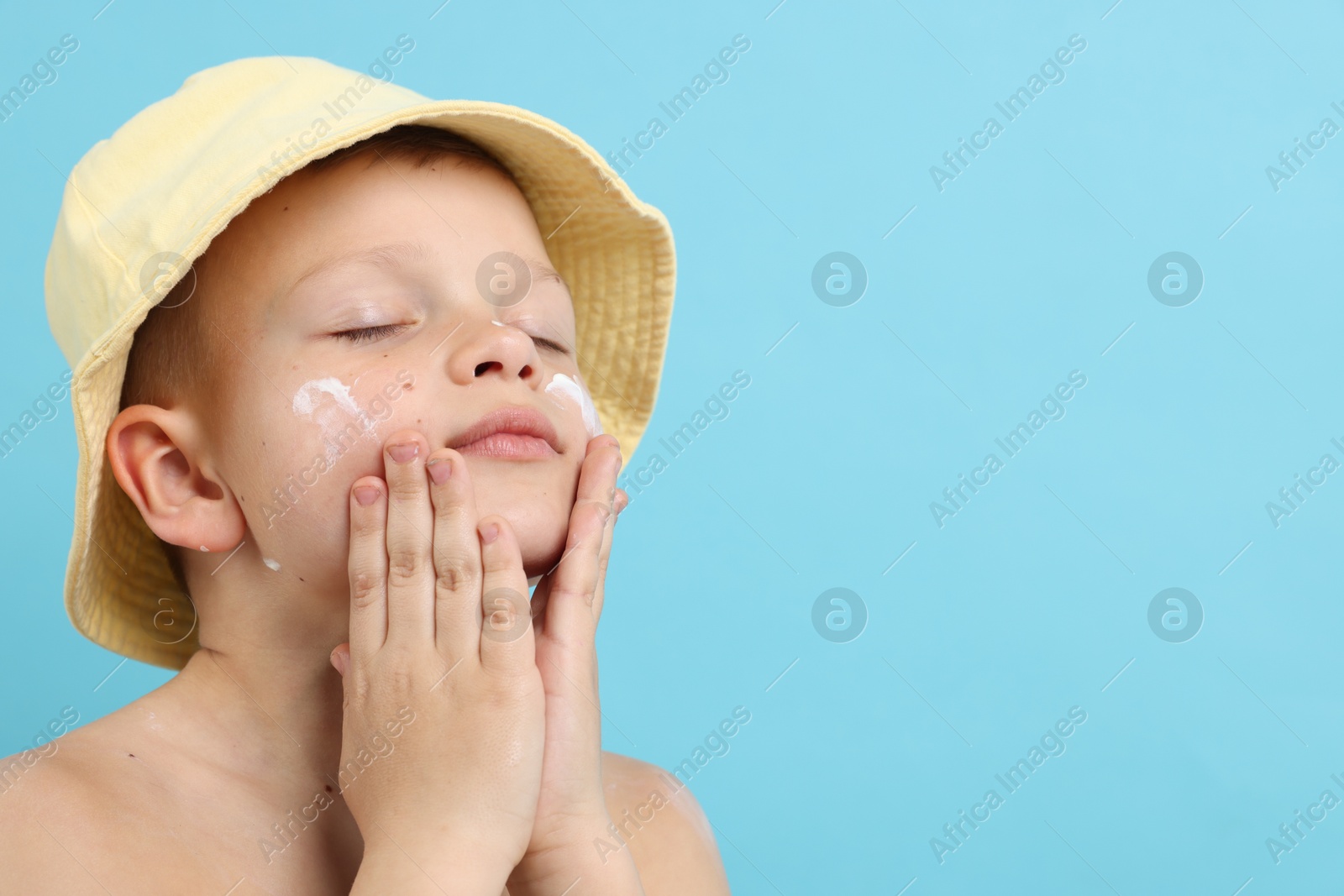 Little boy applying sun protection cream onto his skin on light blue background, space for text Photo of Little boy applying sun protection cream onto his skin on light blue background, space for text