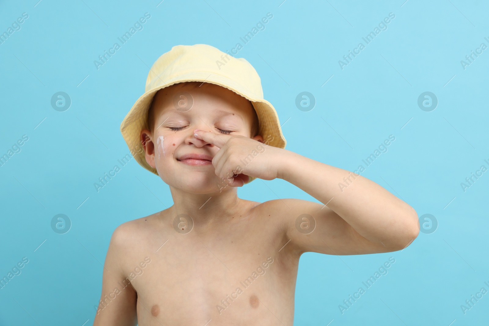 Little boy applying sun protection cream onto his skin on light blue background Photo of Little boy applying sun protection cream onto his skin on light blue background