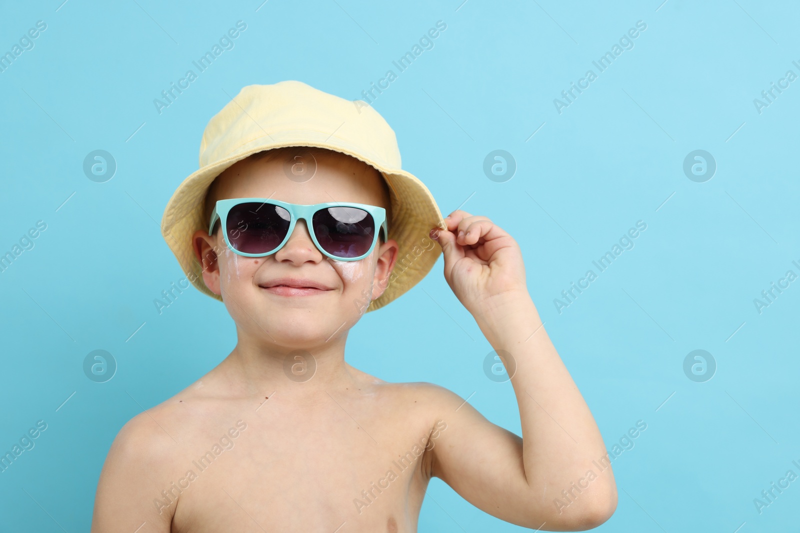 Little boy with sun protection cream on his skin against light blue background Photo of Little boy with sun protection cream on his skin against light blue background