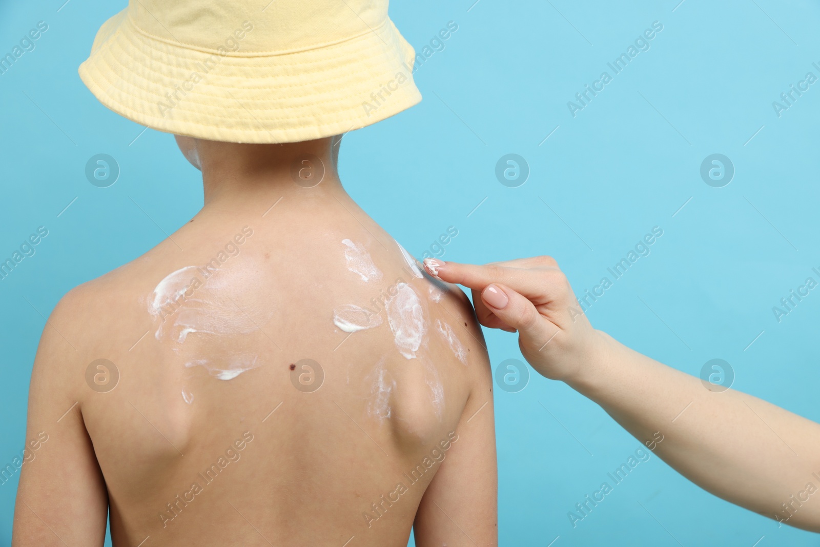 Mother applying sun protection cream onto her son's skin on light blue background, closeup Photo of Mother applying sun protection cream onto her son's skin on light blue background, closeup