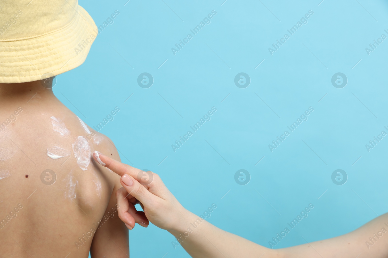 Mother applying sun protection cream onto her son's skin on light blue background, closeup Photo of Mother applying sun protection cream onto her son's skin on light blue background, closeup