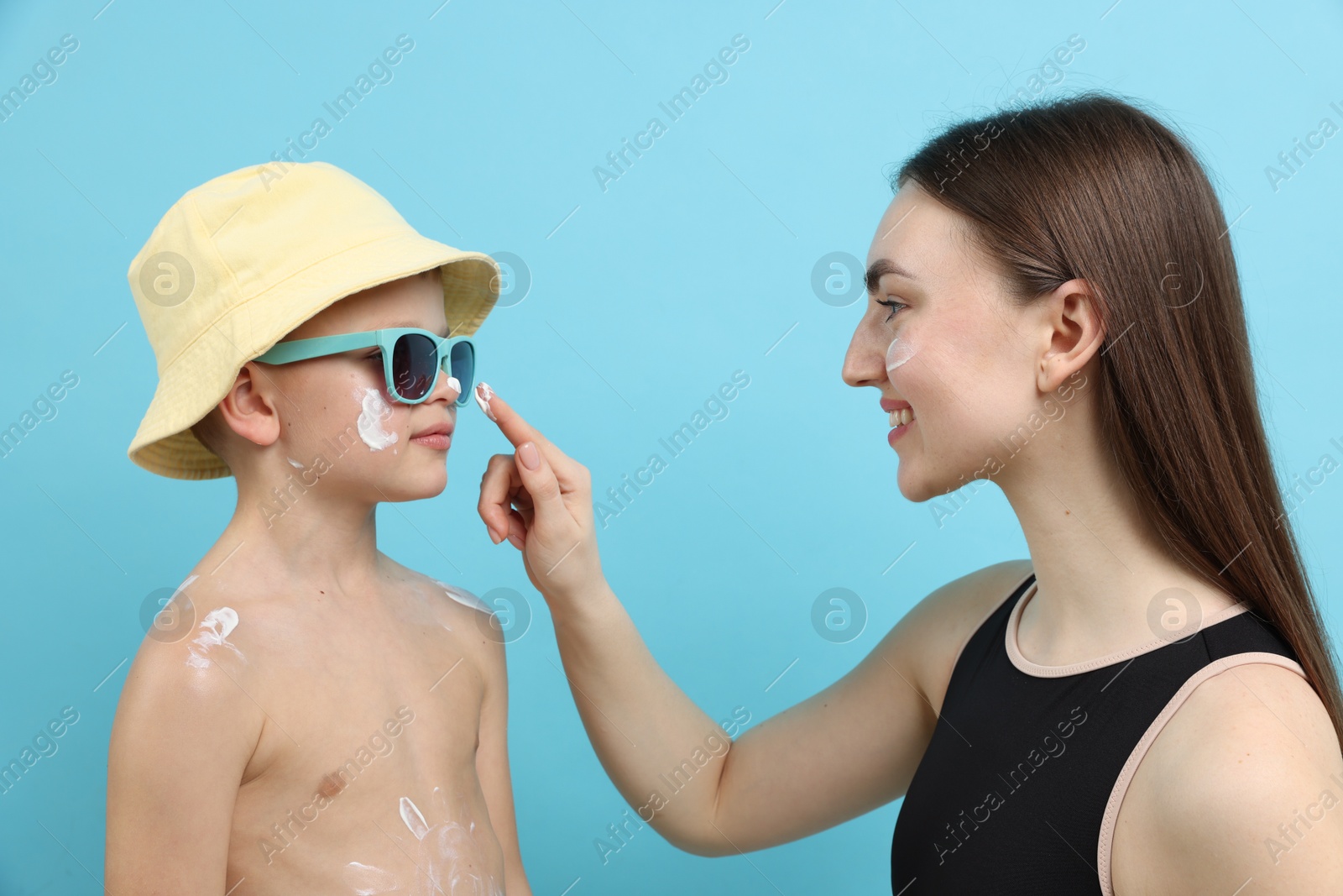 Mother applying sun protection cream onto her son's skin on light blue background Photo of Mother applying sun protection cream onto her son's skin on light blue background
