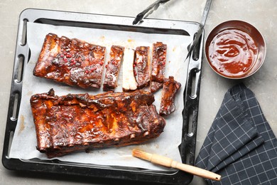 Photo of Delicious spare ribs, sauce and brush on grey textured table, flat lay