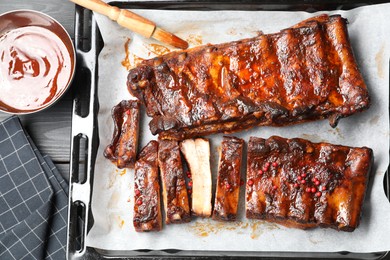 Photo of Delicious spare ribs, sauce and brush on grey wooden table, flat lay