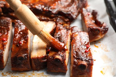 Photo of Spreading sauce with brush onto delicious spare ribs at parchment paper, closeup