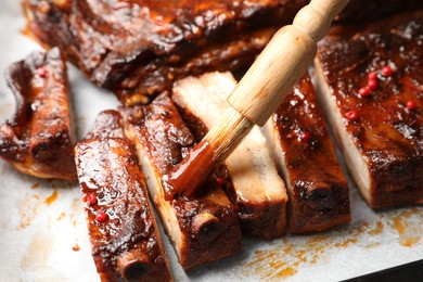 Photo of Spreading sauce with brush onto delicious spare ribs at parchment paper, closeup