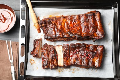 Photo of Delicious spare ribs, sauce and brush on grey wooden table, flat lay