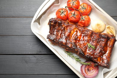 Photo of Delicious spare ribs, rosemary, baked onion and sun dried tomatoes on grey wooden table, top view. Space for text