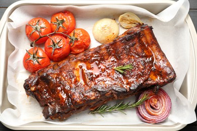 Photo of Delicious spare ribs, rosemary, baked onion and sun dried tomatoes in baking tray, top view