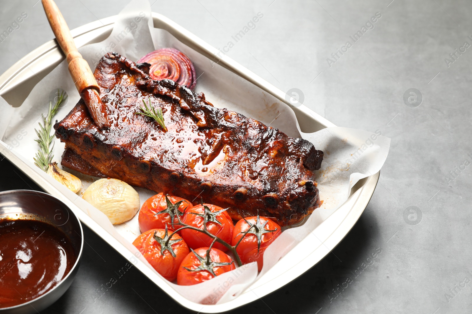 Delicious spare ribs, baked onion, sun dried tomatoes and sauce on grey table, closeup Photo of Delicious spare ribs, baked onion, sun dried tomatoes and sauce on grey table, closeup