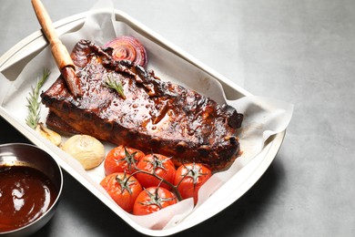 Photo of Delicious spare ribs, baked onion, sun dried tomatoes and sauce on grey table, closeup