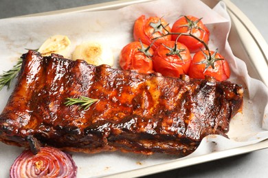 Photo of Delicious spare ribs, rosemary, baked onion and sun dried tomatoes on grey table, closeup