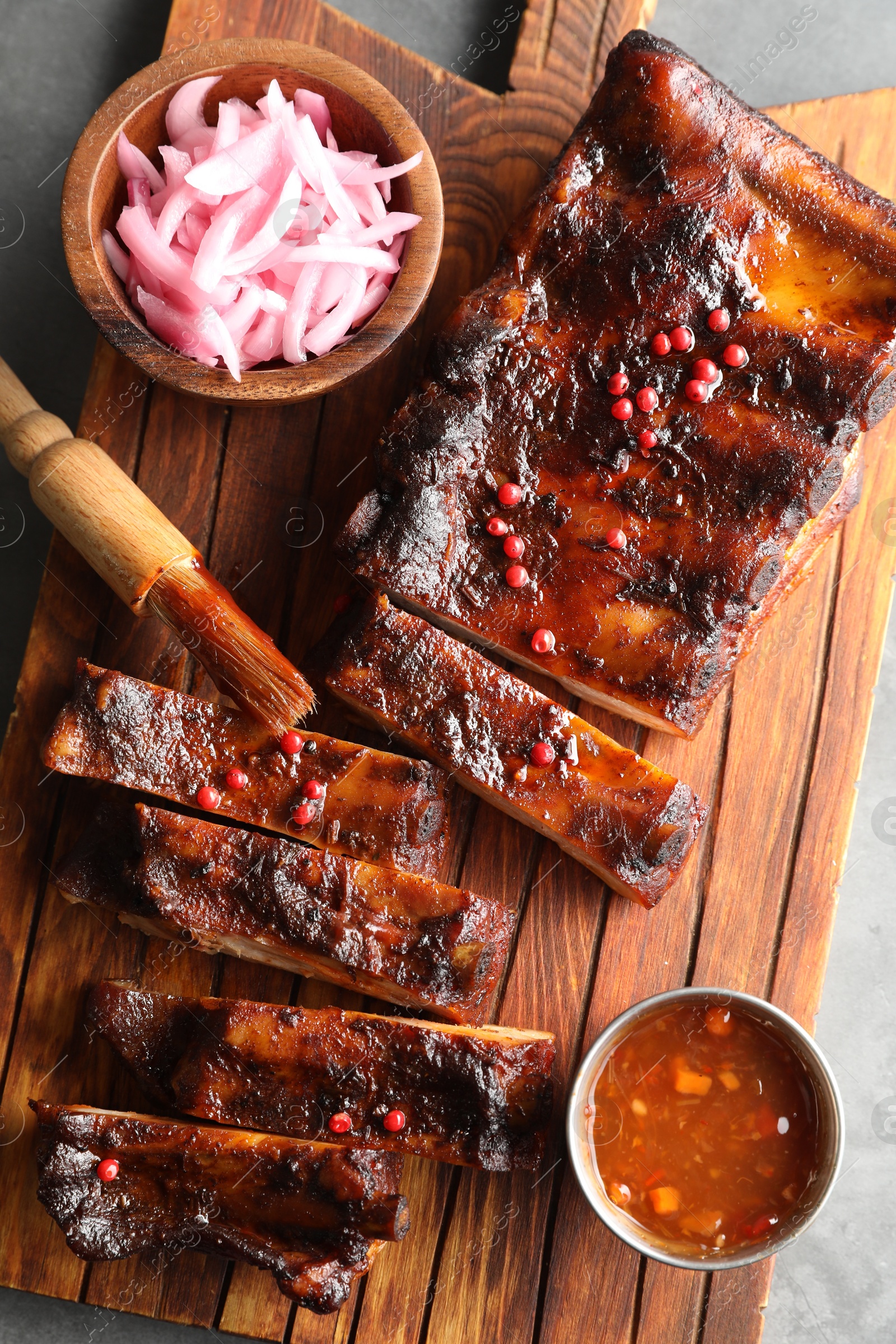 Photo of Delicious spare ribs, onion and sauce on grey table, top view