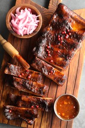 Photo of Delicious spare ribs, onion and sauce on grey table, top view