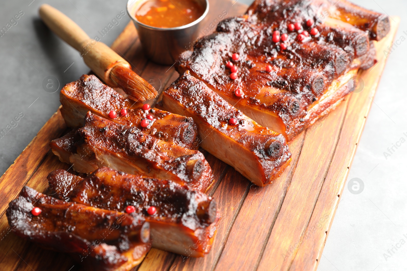 Delicious spare ribs, sauce and brush on grey table, closeup Photo of Delicious spare ribs, sauce and brush on grey table, closeup