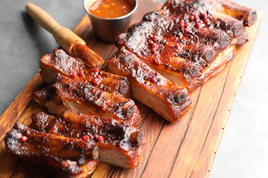 Photo of Delicious spare ribs, sauce and brush on grey table, closeup