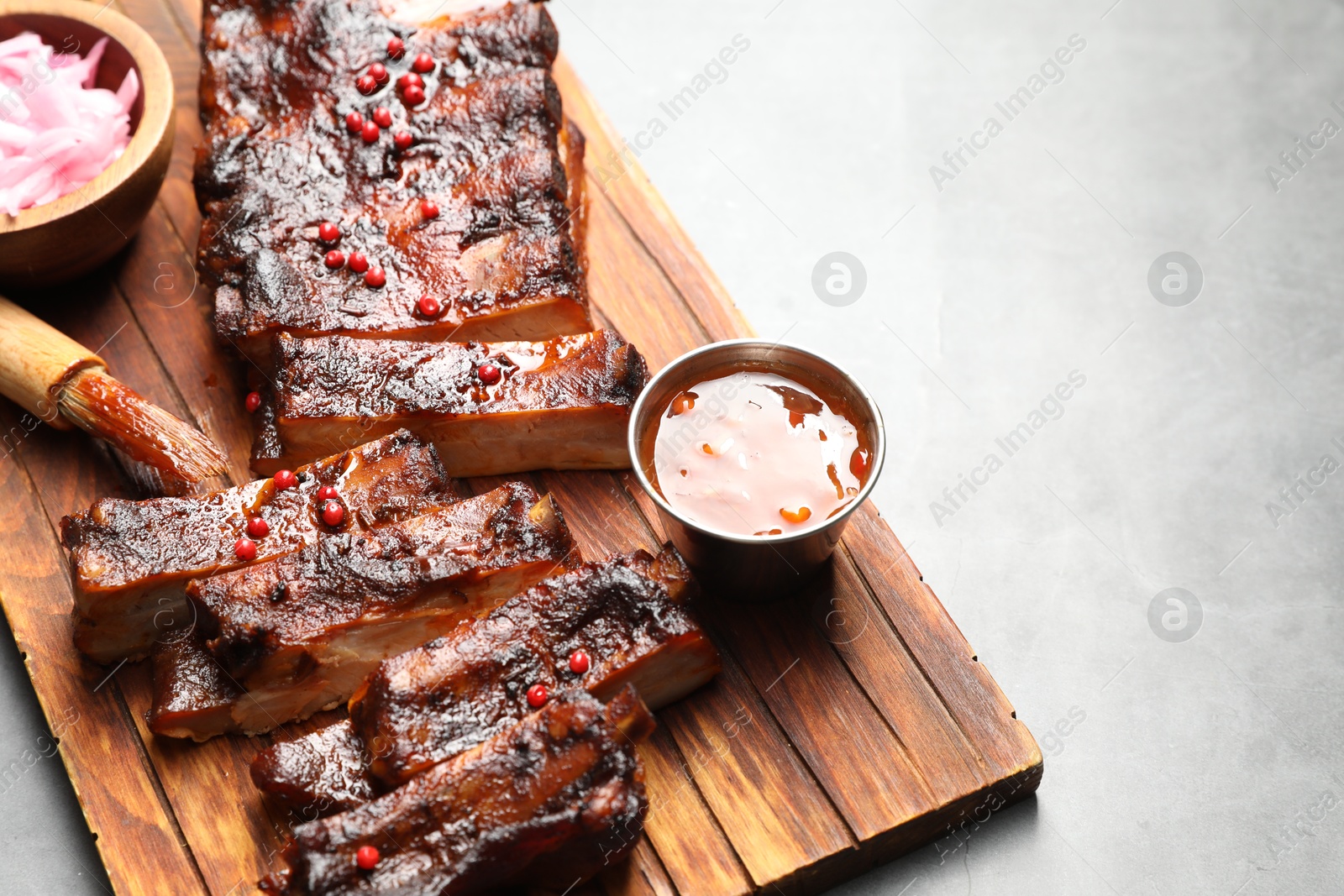 Delicious spare ribs, sauce and brush on grey table. Space for text Photo of Delicious spare ribs, sauce and brush on grey table. Space for text