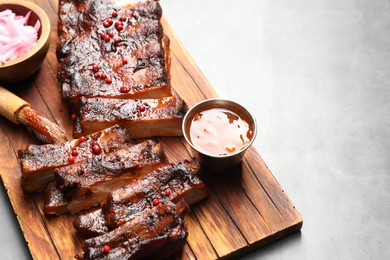 Photo of Delicious spare ribs, sauce and brush on grey table. Space for text