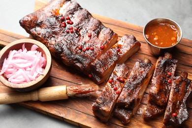 Photo of Delicious spare ribs, onion, sauce and brush on grey table