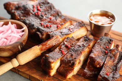 Photo of Delicious spare ribs, onion, sauce and brush on grey table, closeup