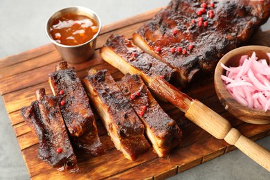 Photo of Delicious spare ribs, onion, sauce and brush on grey table