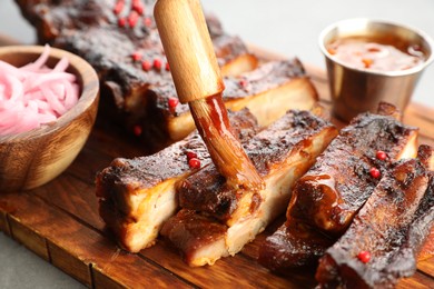 Photo of Spreading sauce with brush onto delicious spare ribs at grey table, closeup