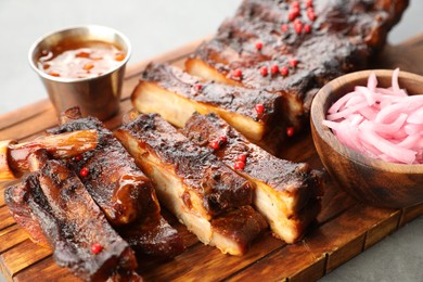 Photo of Delicious spare ribs, sauce and onion on grey table, closeup