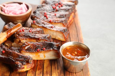 Photo of Delicious spare ribs, sauce and brush on grey table, closeup