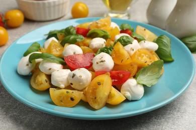 Photo of Tasty salad with yellow tomatoes, basil and mozzarella cheese on light grey table, closeup