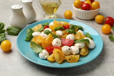Photo of Tasty salad with yellow tomatoes, basil and mozzarella cheese on light grey table, closeup