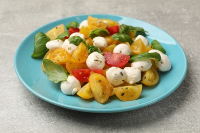 Photo of Tasty salad with yellow tomatoes, basil and mozzarella cheese on light grey table, closeup