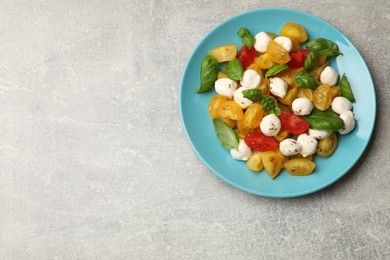 Photo of Tasty salad with yellow tomatoes, basil and mozzarella cheese on light grey table, top view. Space for text