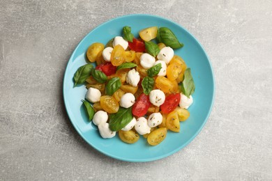 Photo of Tasty salad with yellow tomatoes, basil and mozzarella cheese on light grey table, top view
