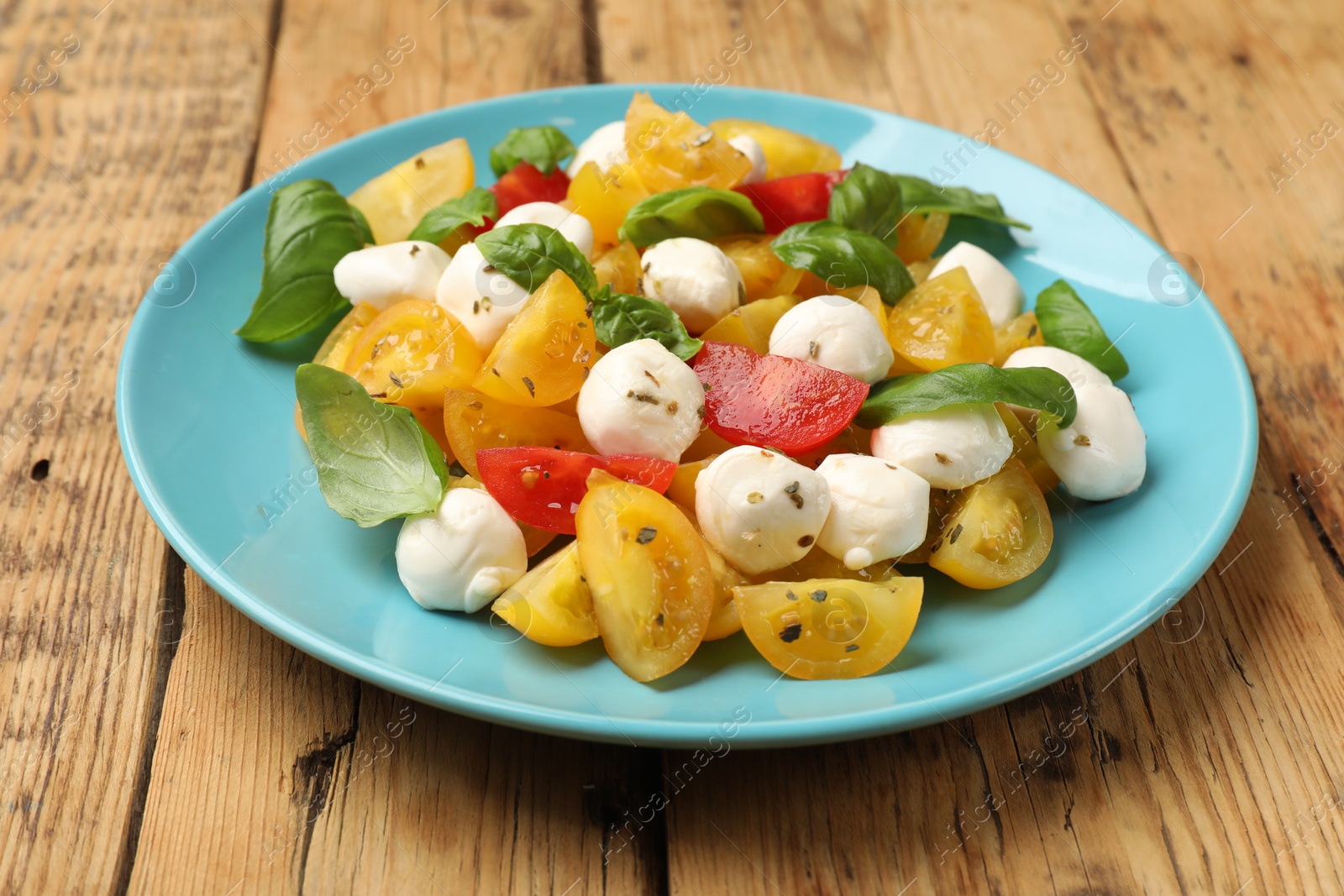Tasty salad with yellow tomatoes, basil and mozzarella cheese on wooden table, closeup Photo of Tasty salad with yellow tomatoes, basil and mozzarella cheese on wooden table, closeup