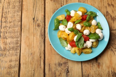 Photo of Tasty salad with yellow tomatoes, basil and mozzarella cheese on wooden table, top view. Space for text