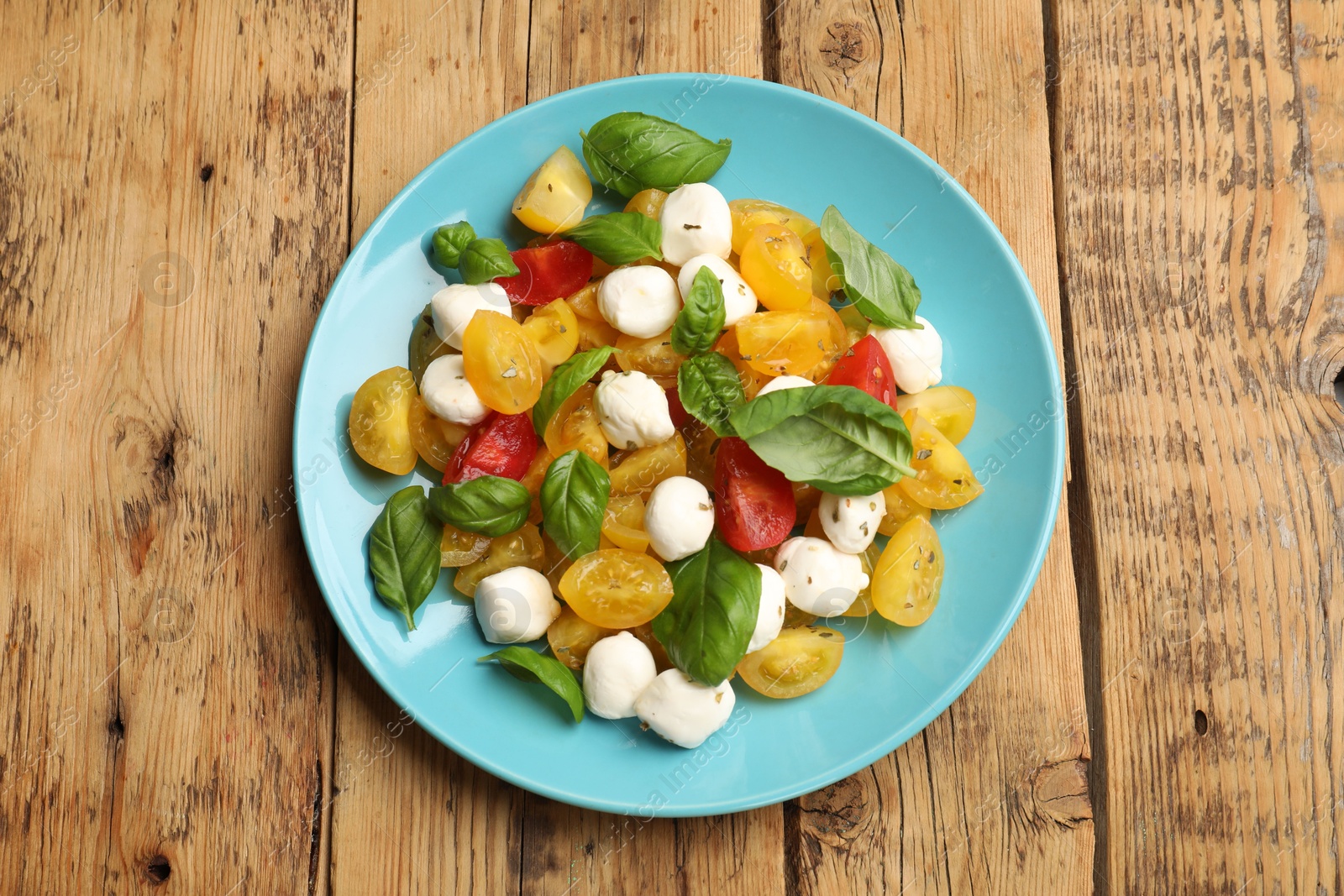 Tasty salad with yellow tomatoes, basil and mozzarella cheese on wooden table, top view Photo of Tasty salad with yellow tomatoes, basil and mozzarella cheese on wooden table, top view