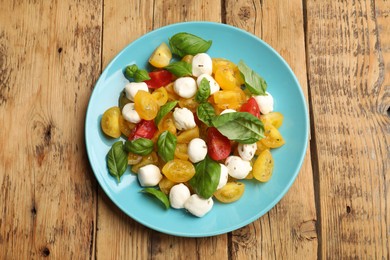 Photo of Tasty salad with yellow tomatoes, basil and mozzarella cheese on wooden table, top view