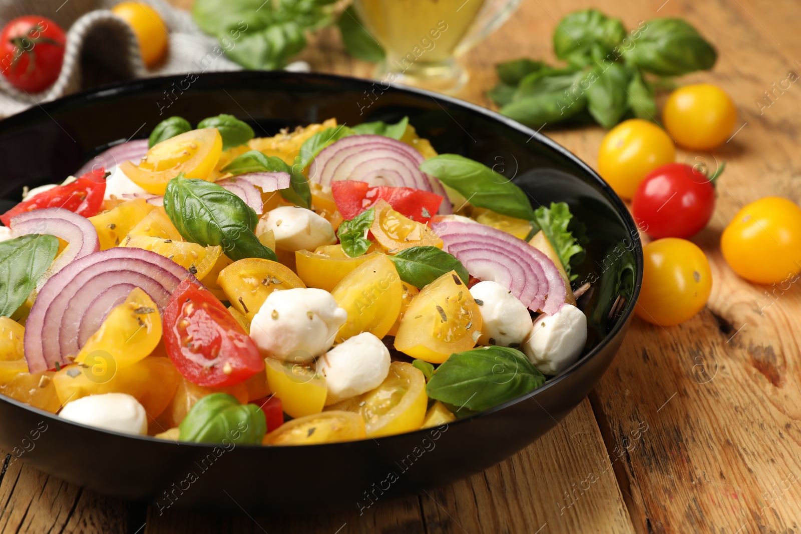 Tasty salad with yellow tomatoes, basil, onion and mozzarella cheese on wooden table, closeup Photo of Tasty salad with yellow tomatoes, basil, onion and mozzarella cheese on wooden table, closeup